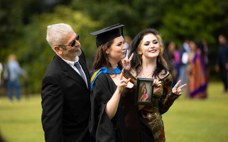 UCD alumna celebrating her graduation with family, holding a framed photo in her hand.
